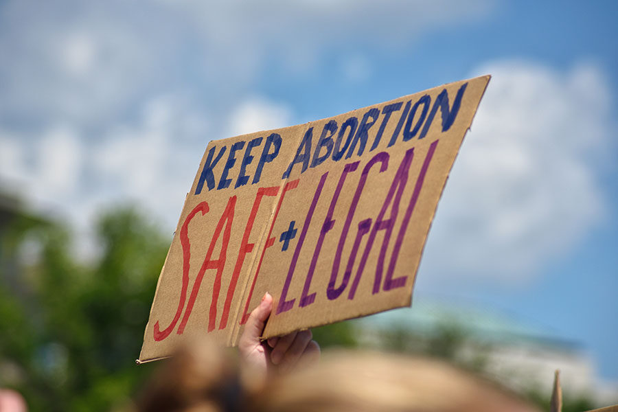 Hand holding sign which reads, "Keep Abortion Safe + Legal"