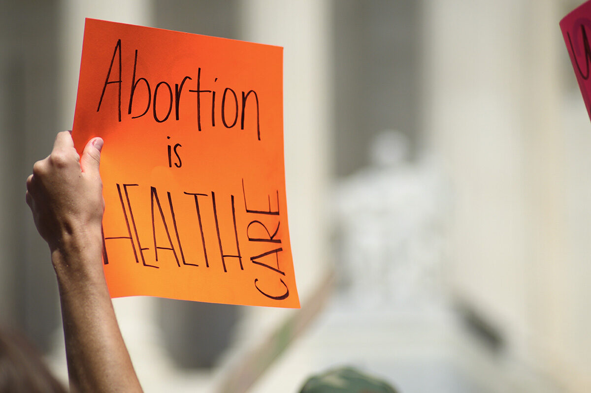 Photo of a hand holding a sign which reads "Abortion is HEALTH CARE"